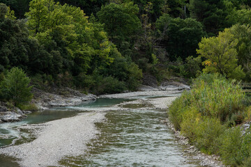 View of a river in South France, flows between rocks and pebbles. It turns right, trees in early autumn colours.