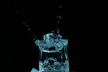 splash of water in a glass by ice cube on black background