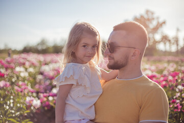 Dad with daughter have fun in peonies field at sunset.