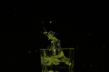 Fototapeta na wymiar splash of water in a glass by ice cube on black background