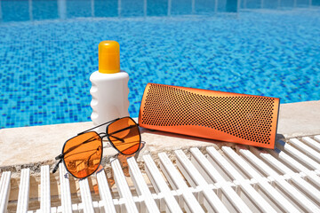 orange coloured beach accessories near swimming pool. Sun cream, sunglasses, music bluetooth speaker
