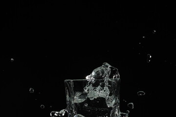 splash of water in a glass by ice cube on black background