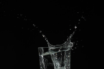 splash of water in a glass by ice cube on black background