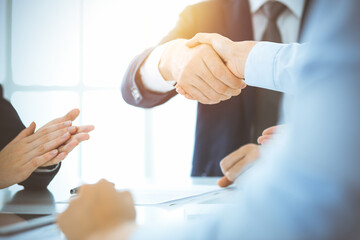 Business people shaking hands finishing up meeting or negotiation in sunny office. Business handshake and partnership concepts