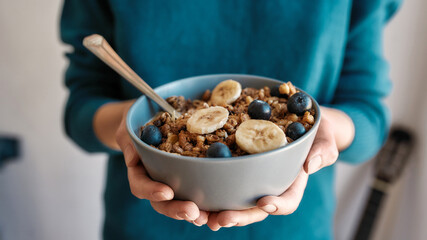 Close up of hands of woman holding homemade granola in a plate with nuts, honey, blueberries,...