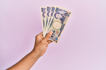 Hispanic hand holding 5000 japanese yen banknotes over isolated pink background.