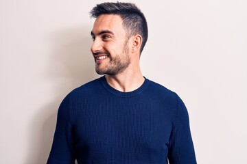 Fototapeta premium Young handsome man with beard wearing casual sweater standing over white background looking to side, relax profile pose with natural face and confident smile.