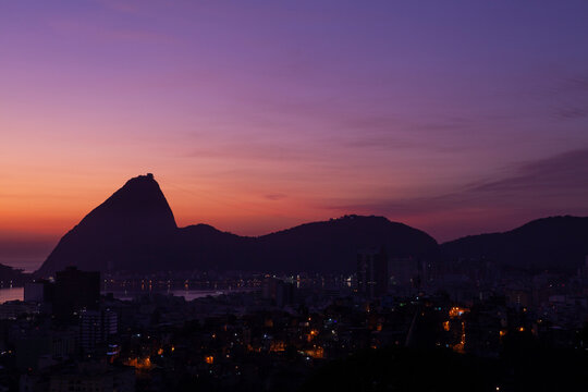 Beautiful distant view of the Sugar Loaf mountain silhouette at sunset against purple sky; Rio de Janeiro, Brazil. Some of the Rio de Janeiro City in the foreground. Copy space for text.