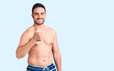 Young handsome man wearing swimwear doing happy thumbs up gesture with hand. approving expression looking at the camera showing success.