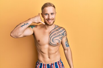 Young caucasian man wearing swimwear shirtless smiling doing phone gesture with hand and fingers like talking on the telephone. communicating concepts.