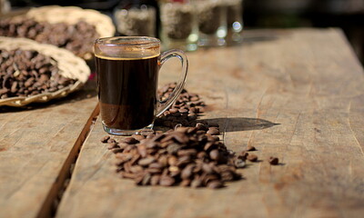 Glass of Black Coffee and roosted coffee beans on the wooden Table