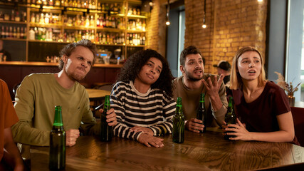 Friends looking disappointed while watching sports match on TV together, drinking beer and cheering for team in the bar. People, leisure, friendship and entertainment concept
