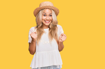 Young blonde girl wearing summer hat celebrating surprised and amazed for success with arms raised and open eyes. winner concept.