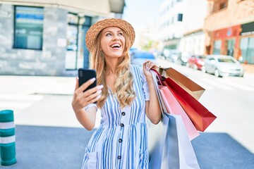 Young beautiful shopper woman smiling happy going to the shops sales holding shopping bags ourtdoors, smiling happy using smartphone