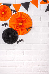 Halloween background. Black and orange paper decorations for Halloween on a white brick wall. Party flags, bats, paper fans. Copy spase, halloween concept. Vertical orientation