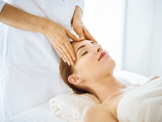 Fototapeta na wymiar Beautiful woman enjoying facial massage with closed eyes in spa center