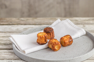 Canelé cake - a small french pastry flavored with rum and vanilla on plate at wooden table.