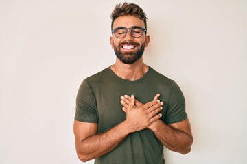 Young hispanic man wearing casual clothes and glasses smiling with hands on chest with closed eyes and grateful gesture on face. health concept. - obrazy, fototapety, plakaty