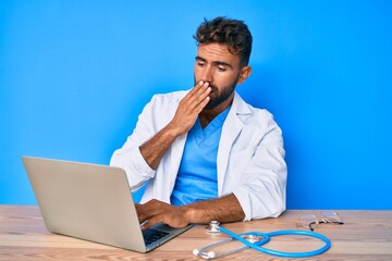 Young hispanic man wearing doctor uniform working at the clinic covering mouth with hand, shocked and afraid for mistake. surprised expression