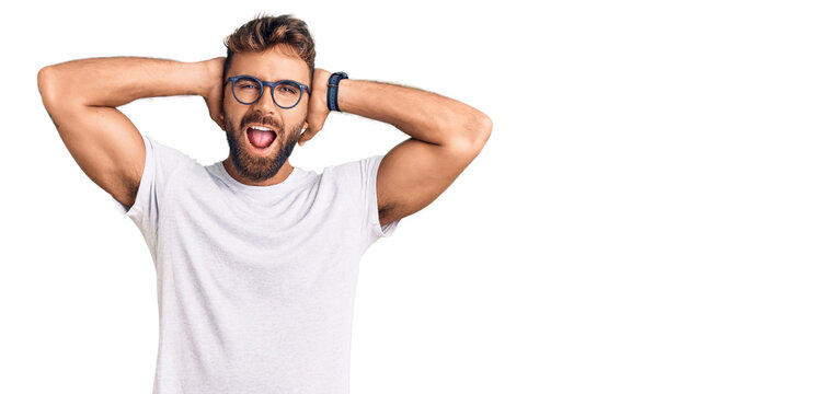 Young hispanic man wearing casual clothes and glasses crazy and scared with hands on head, afraid and surprised of shock with open mouth