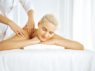 Obraz na płótnie Canvas Beautiful blonde woman enjoying back massage with closed eyes. Spa salon concept