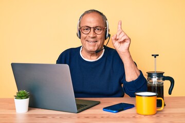 Senior handsome man with gray hair working at the office wearing operator headset surprised with an...