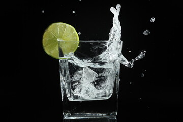 splash of water with lime in a glass over ice cube on black background