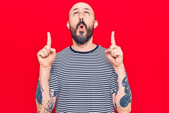 Young handsome man wearing casual clothes amazed and surprised looking up and pointing with fingers and raised arms.