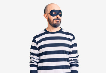 Young handsome man wearing burglar mask smiling looking to the side and staring away thinking.