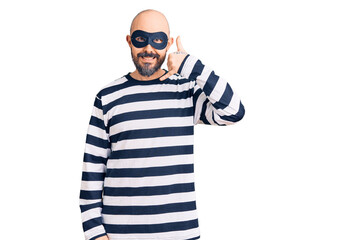 Young handsome man wearing burglar mask smiling doing phone gesture with hand and fingers like talking on the telephone. communicating concepts.