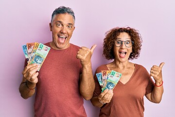 Beautiful middle age couple holding australian dollars pointing thumb up to the side smiling happy with open mouth © Krakenimages.com
