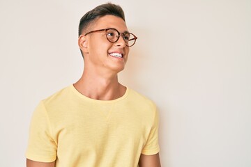 Young hispanic boy wearing casual clothes and glasses looking away to side with smile on face, natural expression. laughing confident.