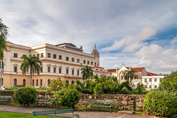 Obraz premium Panama City, Panama - November 30, 2008: Large government building and tower and entrance of Sanctuario de la Esperanza part of San Francisco de Asis church under cloudscape. Simon Bolivar Square.