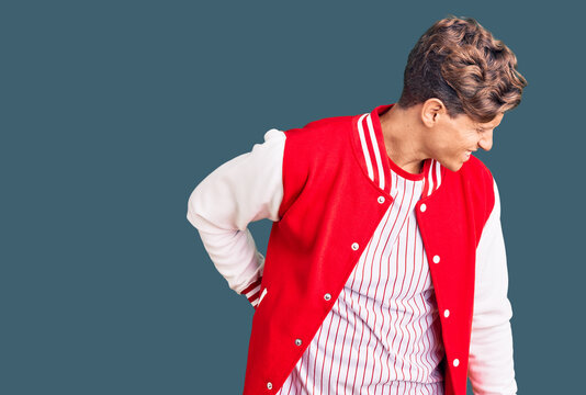 Young handsome man wearing baseball uniform suffering of backache, touching back with hand, muscular pain