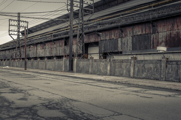 Fototapeta na wymiar Looking down a wore out empty street next to an abandoned industrial factory with crumbling exterior in the midwest