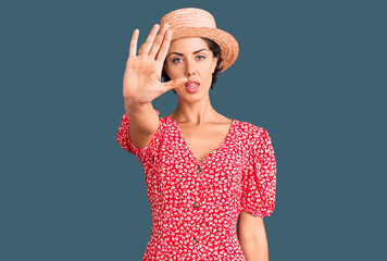 Young beautiful woman wearing summer hat doing stop sing with palm of the hand. warning expression with negative and serious gesture on the face.