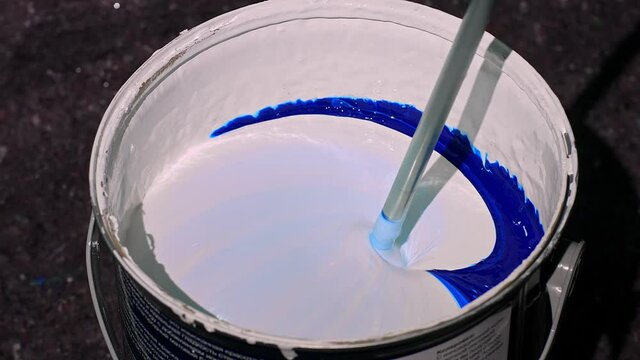 The process of mixing the blue paint in a bucket with a mixer. Mixing paint in a barrel, mixing paint in a factory, Factory automatic color mixing. Mixing blue paint in a factory. 4K FOOTAGE. Close-up