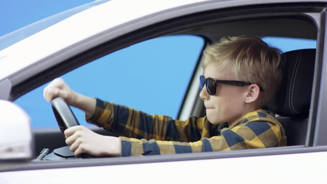A little blonde boy in casual clothes is travelling. Handsome boy is driving car with greenscreen background. He is sitting in the car. He is listening to the music and dancing