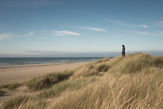 Woman in blue dress standing in dunes by sea