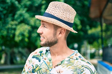 Handsome caucasian man wearing summer hat and flowers shirt smiling happy outdoors