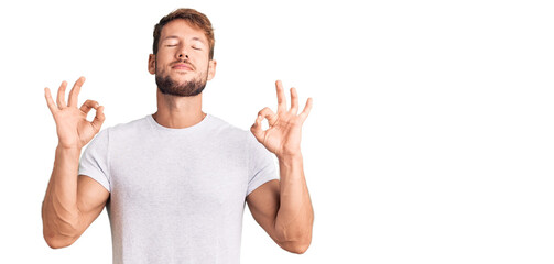 Young caucasian man wearing casual white tshirt relax and smiling with eyes closed doing meditation gesture with fingers. yoga concept.