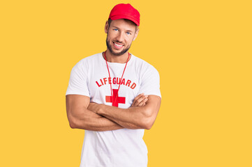 Young caucasian man wearing lifeguard t shirt holding whistle happy face smiling with crossed arms...