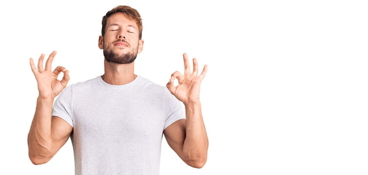Young caucasian man wearing casual white tshirt relax and smiling with eyes closed doing meditation gesture with fingers. yoga concept.