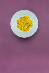 Rice recipe with vegetables and fish on a white circle plate served on a textured purple tablecloth and space to input a text. Spanish paella background.