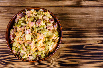 Salad with sausage, green pea, onion and carrot in glass bowl on wooden table. Top view