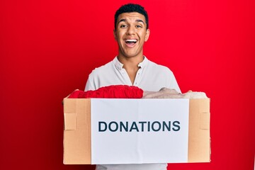 Young arab man holding donation box with clothes smiling and laughing hard out loud because funny crazy joke.