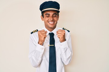 Young hispanic man wearing airplane pilot uniform excited for success with arms raised and eyes closed celebrating victory smiling. winner concept.