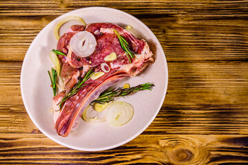 Raw ribeye steak, spices, rosemary, onion and garlic in a ceramic plate on wooden table. Top view