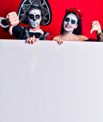 Young couple wearing mexican day of the dead costume holding blank empty banner with angry face, negative sign showing dislike with thumbs down, rejection concept