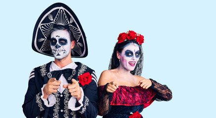 Young couple wearing mexican day of the dead costume over background pointing fingers to camera with happy and funny face. good energy and vibes.